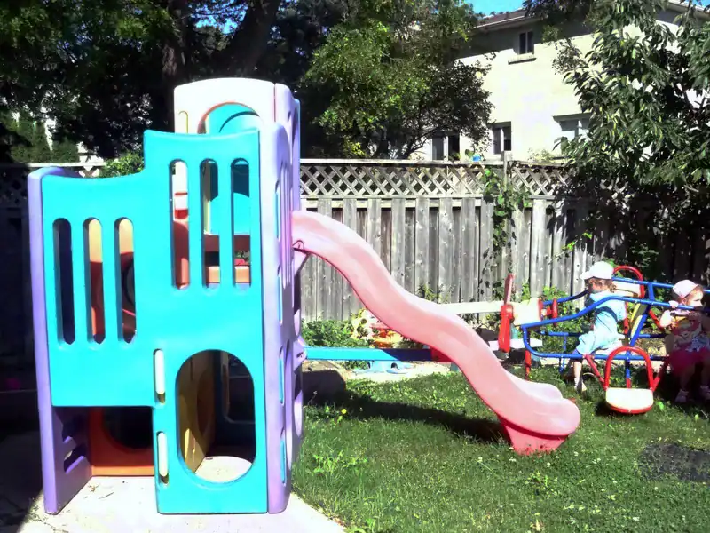 Gallery 10 Children playing on a slide and rocking toys in a vibrant outdoor playground at Diana Daycare Newmarket, featuring age-appropriate play structures and safe environment.