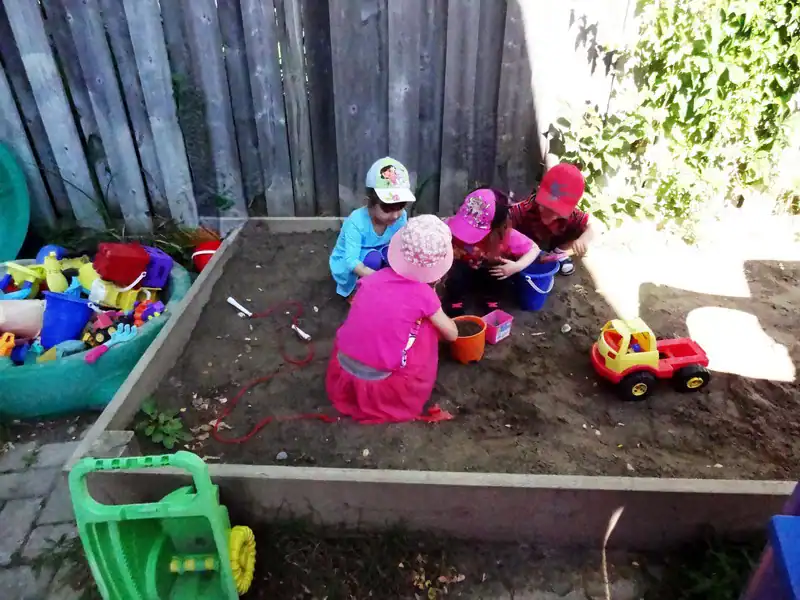 Gallery 3 Kids playing in outdoor sandbox with toys, gardening tools, and colorful activities at Diana Daycare.
