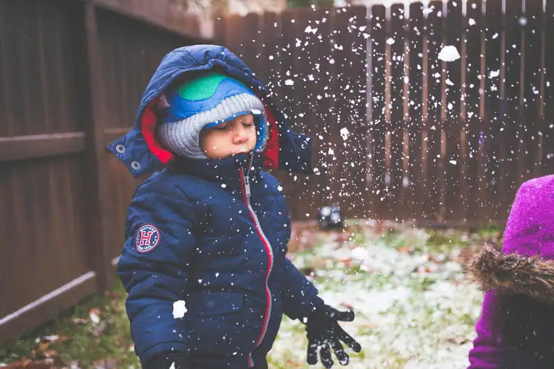 Young child playing in the snow, bundled up in a navy jacket and winter accessories.